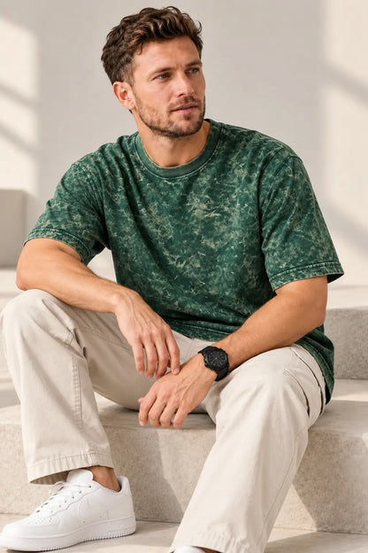 Man seated wearing a green acid wash oversized t-shirt with beige trousers and white sneakers