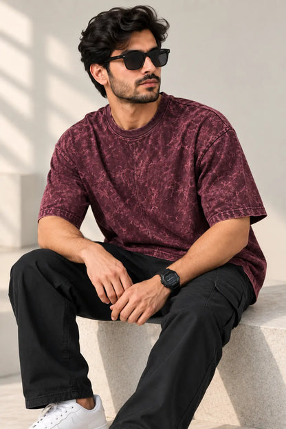 Man seated wearing a maroon acid wash oversized t-shirt with black cargos and white sneakers