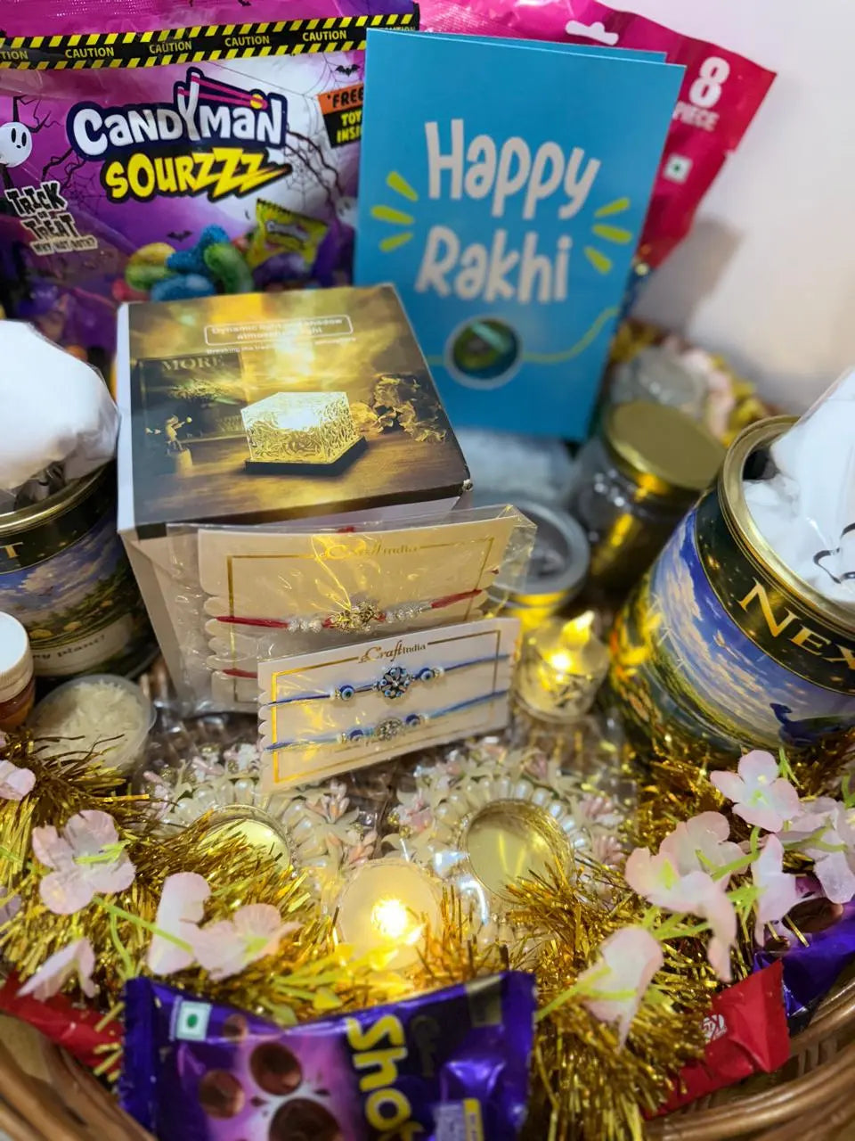 Close-up of Ultimate Rakhi Celebration Hamper contents including designer Rakhis, greeting card, surprise necklace, decorative night lamp, chocolates, and festive essentials.